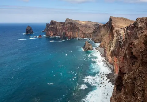 Red cliffs and blue water at Ponta de São Lourenço, the exposed coastal scenery of the peninsula walk.
